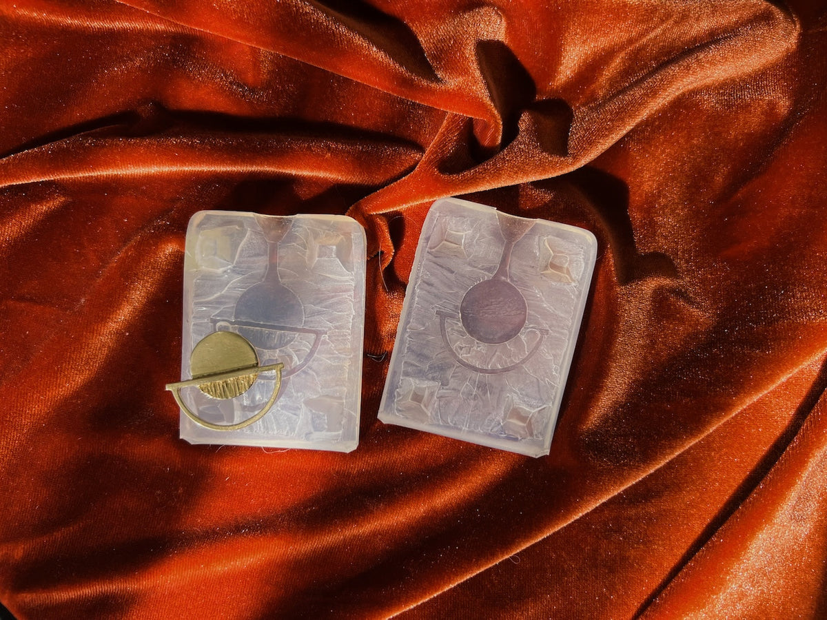 a photo of a hand holding a 2 rings. one ring is made out of pink wax and the other is made from brass. They show the process of lost wax casting to create multiples