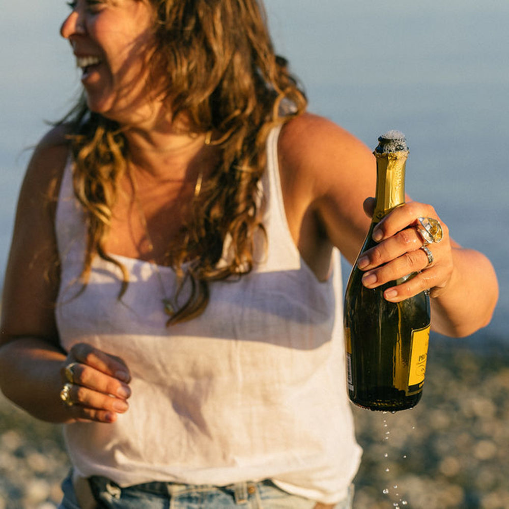 a woman, Rebekah Jaramillo, laughing and holding a bottle of champagne that's bubbling over