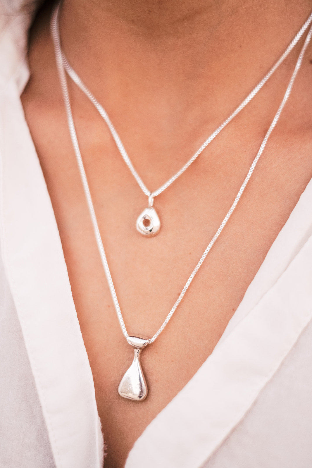 A focused photo of a woman neckline wearing two silver necklaces and a white shirt