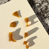 Six small wax carved charms arranged on a cream textured tile, with rough stone visible around the edges and strong sunlight casting sharp shadows.