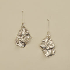 Pair of silver textured earrings on a beige background