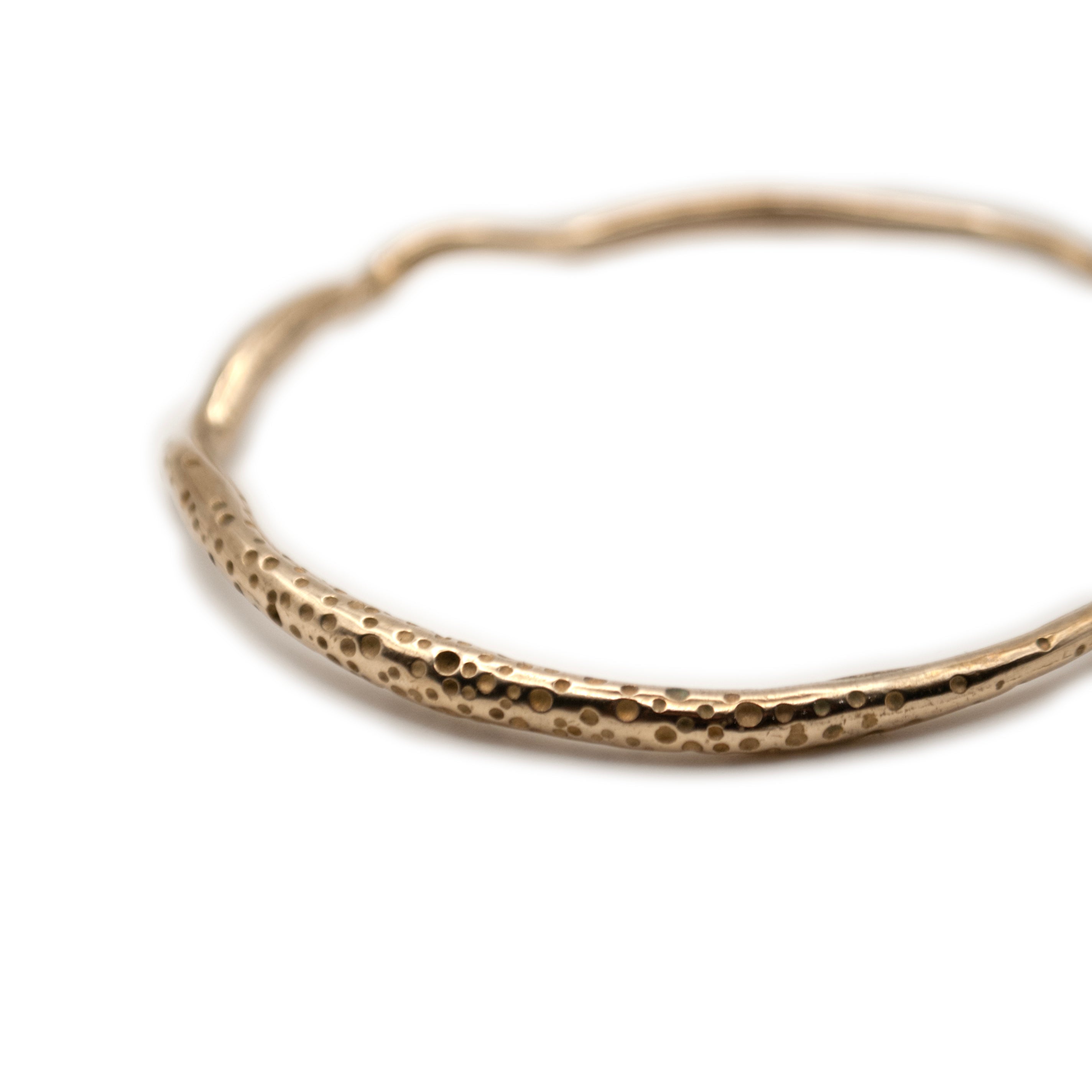 A gold-colored bracelet with a textured, sea urchin-like pattern, displayed against a white background.