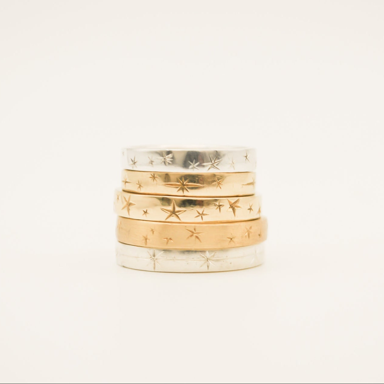 Stack of gold rings with engraved patterns on a light beige background