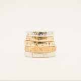 Stack of gold rings with engraved patterns on a light beige background